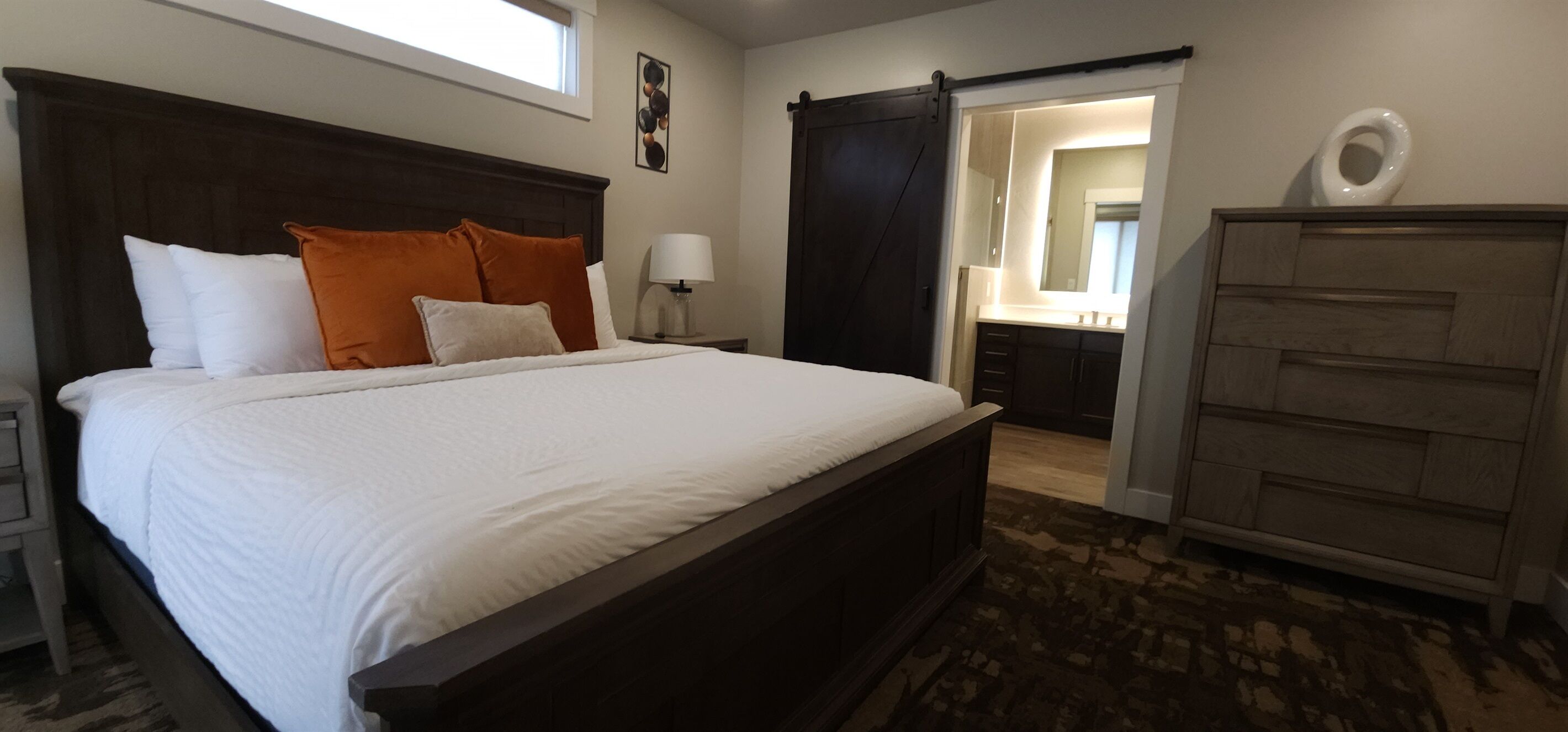 Een slaapkamer met een groot bed, een nachtkastje, een dressoir en een schuifdeur naar een badkamer.