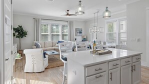Ein geräumiges Wohnzimmer mit einem großen weißen Sofa, einem Essbereich mit einer weißen Kochinsel und einem Deckenventilator.