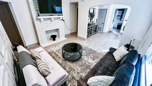 A modern living room with a white brick fireplace, a flat-screen TV mounted above it, a round coffee table, and a sofa with striped cushions. - Beautiful Apartment In Downtown Baltimore (Baltimore)