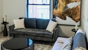 A modern living room with a grey sofa, a round black coffee table, and a white sofa. There is a large abstract painting on the wall and a window with blinds. - Beautiful Apartment In Downtown Baltimore (Baltimore)