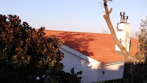 Un jardin planté d’arbres et d’arbustes devant un bâtiment surmonté d’un toit recouvert de tuiles rouges.