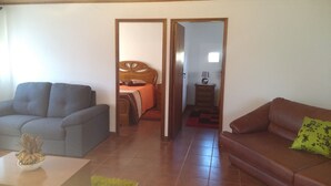 Un salon avec un canapé gris, un canapé marron, une table basse et un lit doté d’une tête de lit en bois.