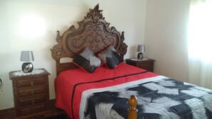 Une chambre à coucher avec une tête de lit en bois, une couvre-lit rouge, deux tables de chevet avec des lampes et une couverture à motifs rouges et noirs.