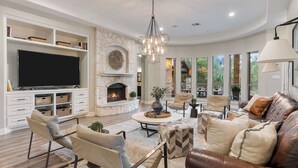 A spacious living room with a fireplace, comfortable seating, and large windows offering a view of the outdoors. - Weekday deals Pool King Bed Giant games Single level Space Firepit Min DT Austin (Austin)