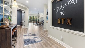 A modern interior with a 'Welcome to ATX' sign, a bar area with stools, and a dining space with chairs. - Weekday deals Pool King Bed Giant games Single level Space Firepit Min DT Austin (Austin)