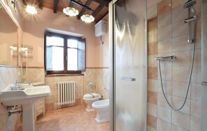 Un bagno con lavandino, due servizi igienici, doccia, finestra e termosifone.
