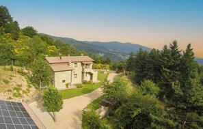 Una casa in pietra con tetto in tegole, circondata da un giardino e con vista su dolci colline.