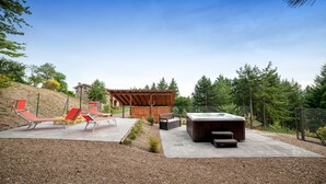 Uma área de terraço ao ar livre com hidromassagem, espreguiçadeiras e uma estrutura de pérgola.