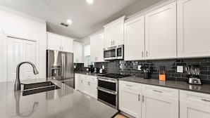 A modern kitchen with white cabinets, stainless steel appliances, and a black tiled backsplash. - 5BR 5BA Home Storey Lake Water Park Amenities (Kissimmee)