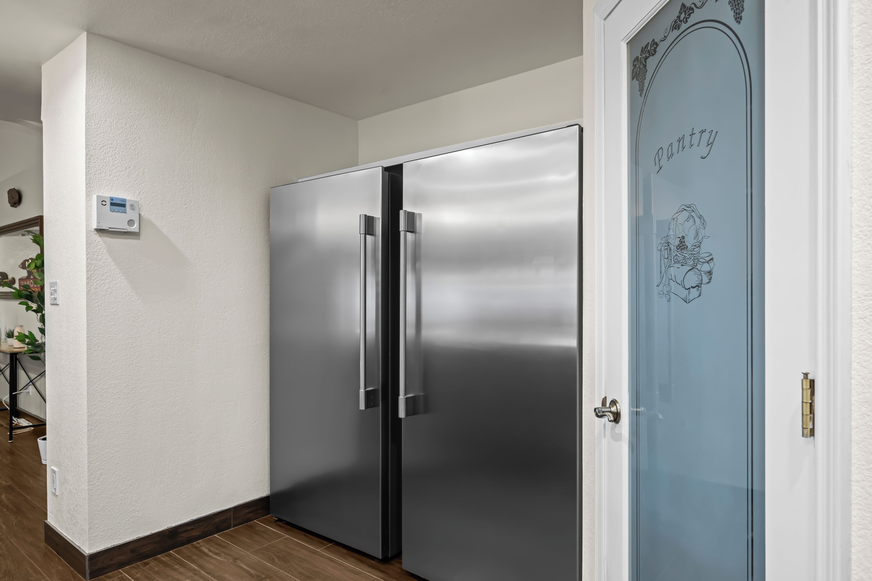 A stainless steel refrigerator in a kitchen with a white wall and a pantry door.