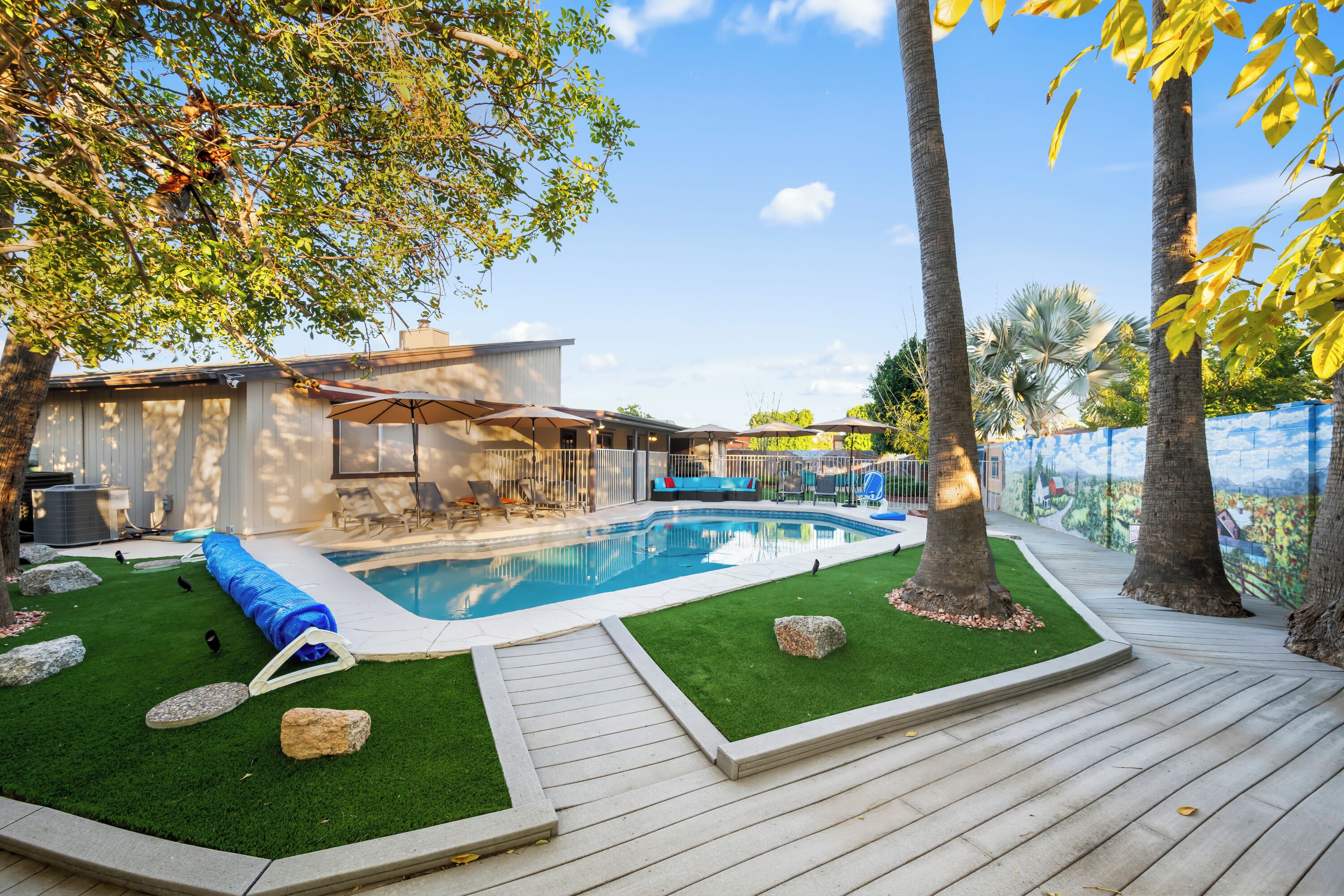 Ein Garten mit Schwimmbad, Kunstgrashalm und einer Holzterrasse.