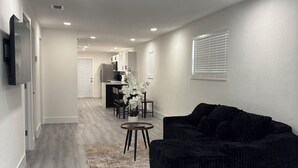 A modern living room with a black sofa, a dining area with a table and chairs, and a kitchen in the background. - La Orquidia (Miami)