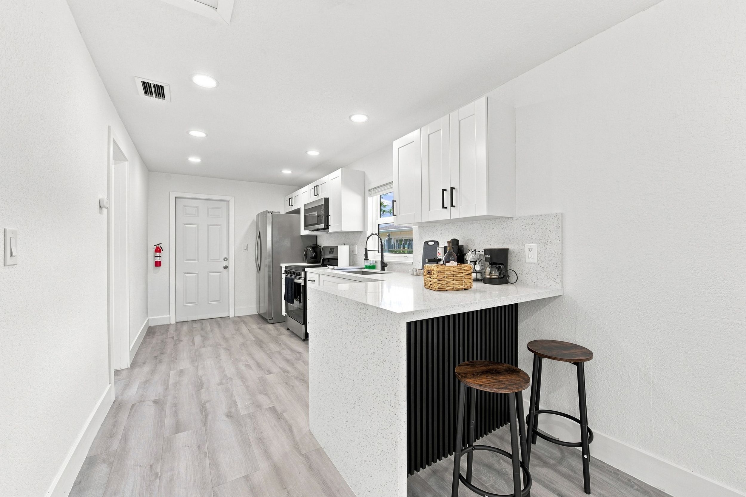 A modern kitchen with white cabinetry, stainless steel appliances, and a bar area with stools.