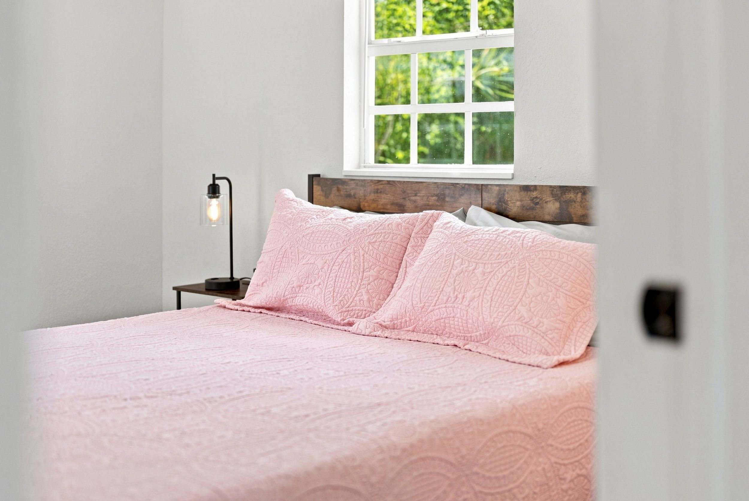 Un dormitorio con cama, mesita de noche, lámpara y ventana con vista a la vegetación.