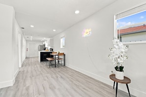 A modern kitchen with white cabinets, a dining area with a wooden table and chairs, and a potted orchid on a small table.