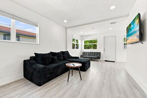 A modern living room with a black sofa, a small round table, and a large flat-screen TV mounted on the wall.