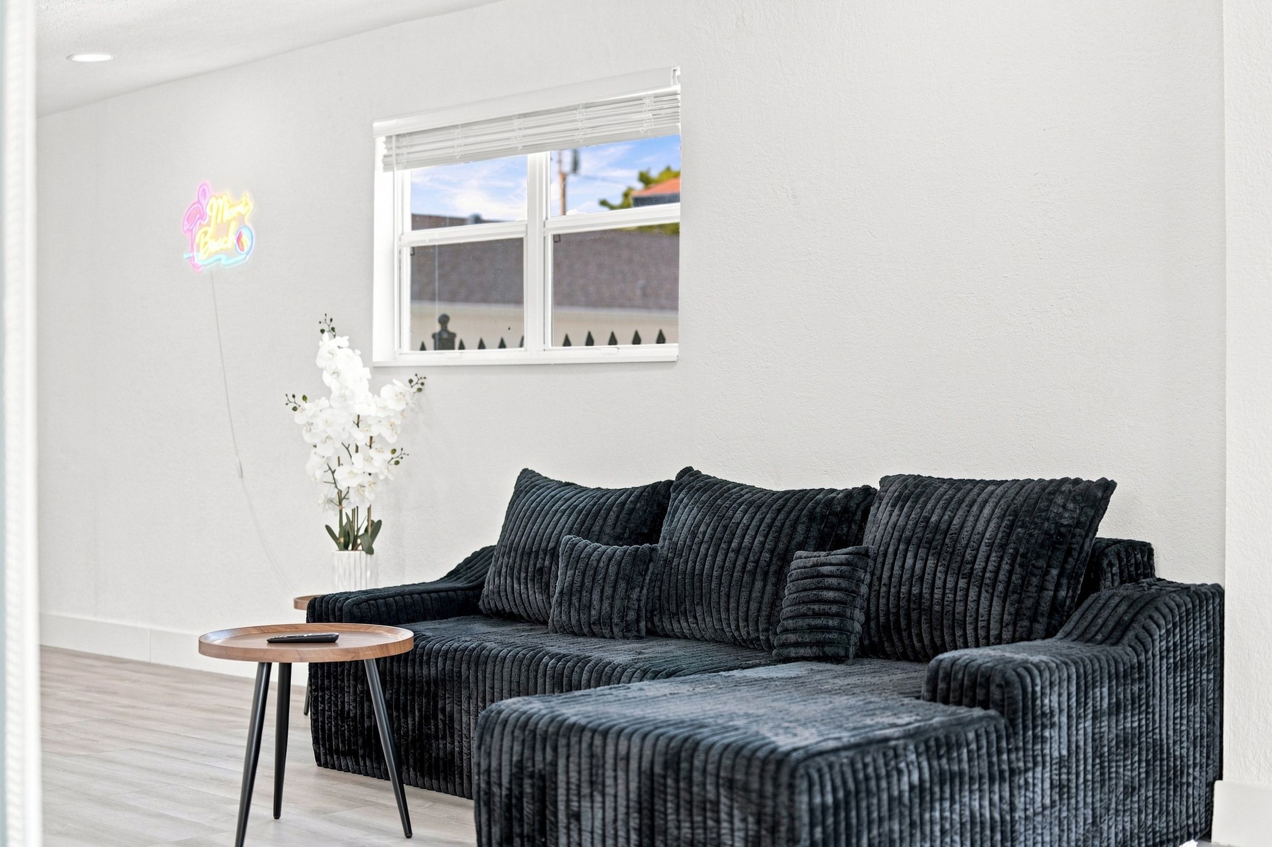 Una sala moderna con un sofá oscuro y texturizado, una mesita redonda de madera y un jarrón blanco con flores.