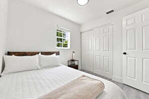 A bedroom with a bed, a nightstand, a window, and a set of white doors.