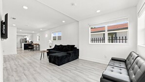 Ein geräumiger Wohnbereich mit einem schwarzen Sofa, einer Ledercouch und einem Esstisch mit Stühlen.