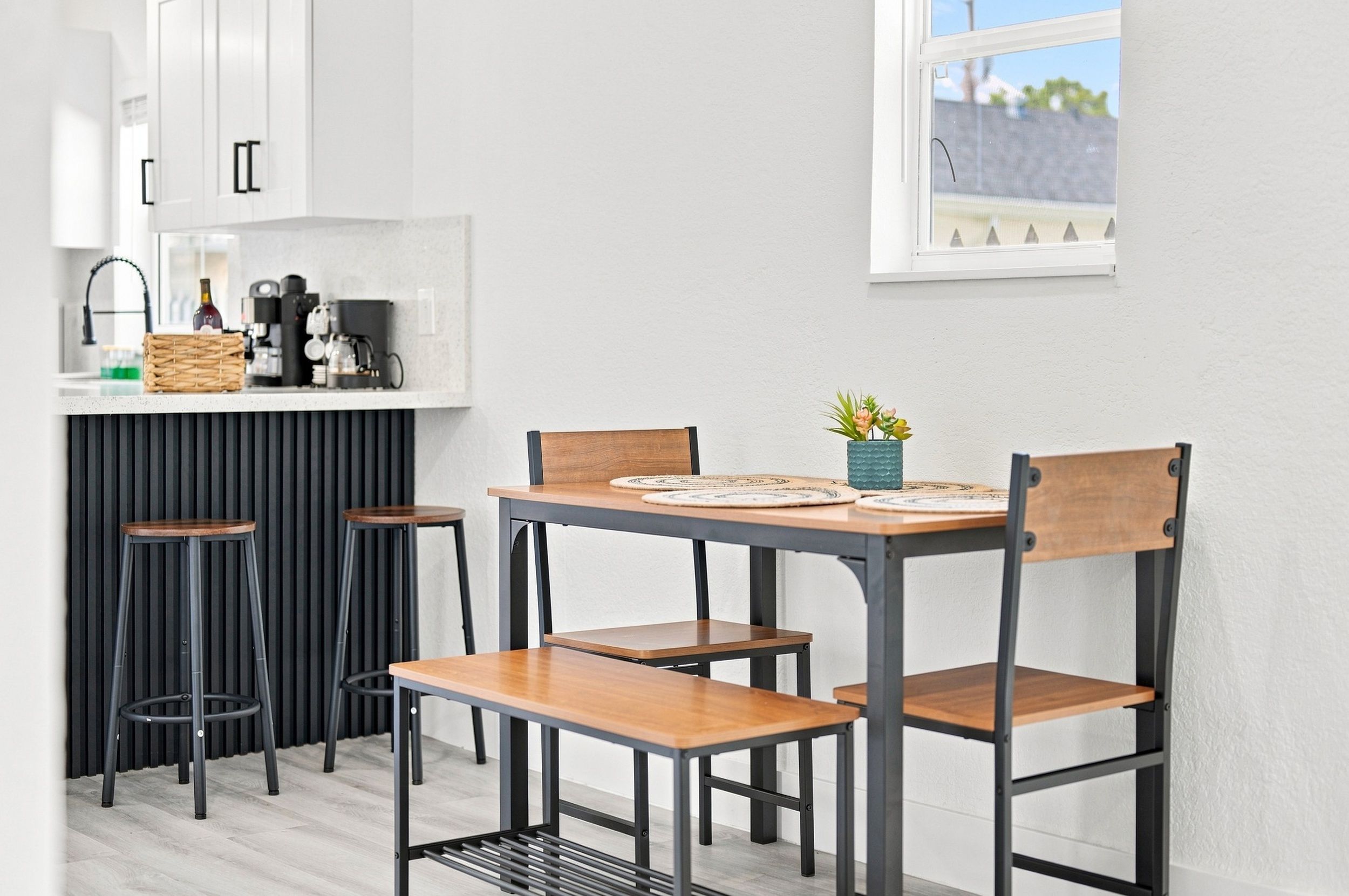 Cocina compacta con comedor, que incluye una mesa central con sillas, una cafetera y una pequeña planta en maceta.