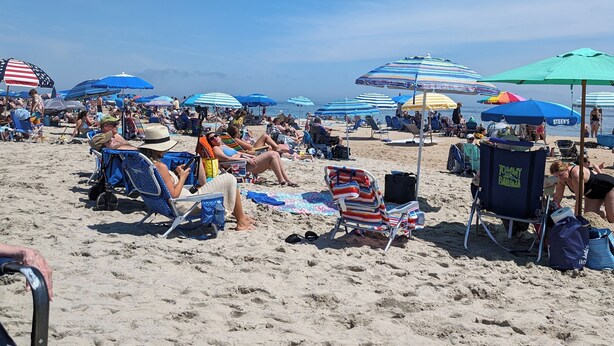 Ein Strand mit vielen Sonnenschirmen und Liegestühlen, der einen öffentlichen Strandabschnitt zeigt.