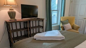 Ein Schlafzimmer mit einem Bett, einem Fernseher auf einem Holzständer, einer Lampe und einem Sessel.