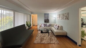 A living room with a sofa, a coffee table, and a large window with blinds. - Charming Bright 3BR House - Upper Level Suite (Burnaby)