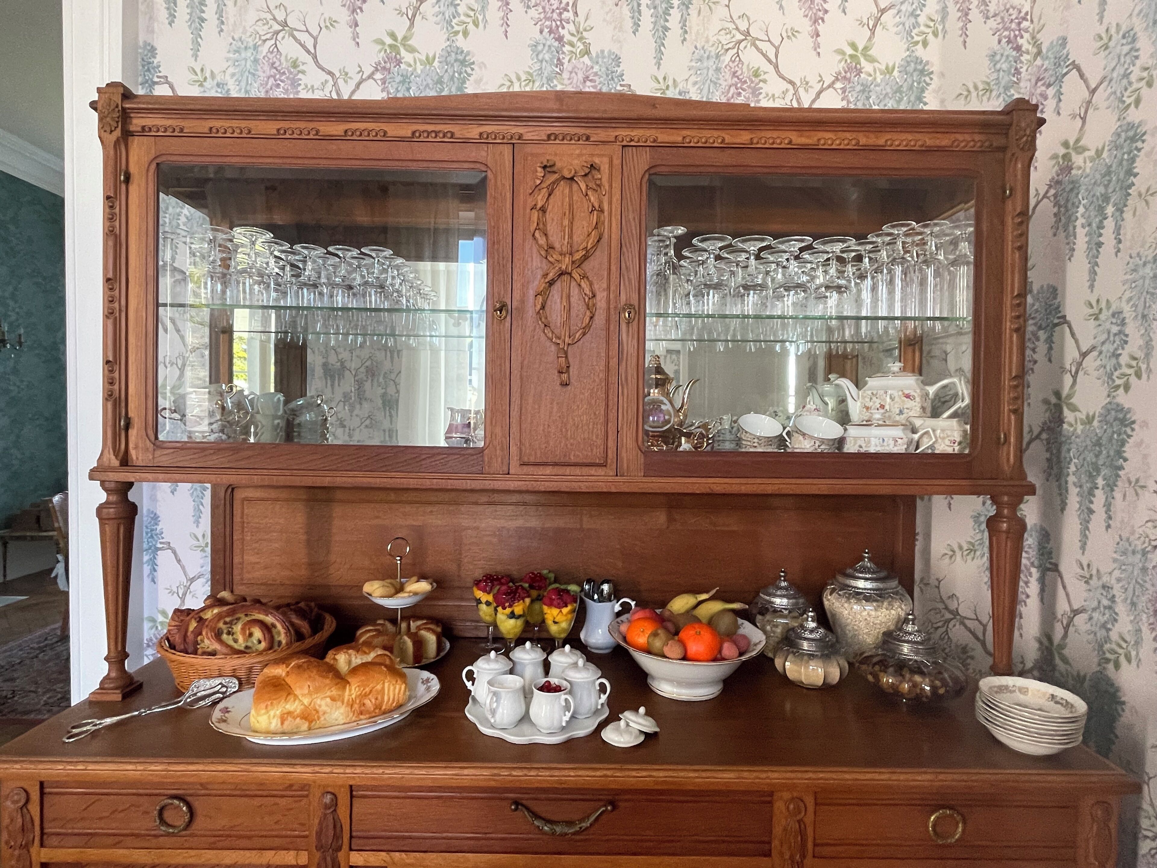 Un bufé de madera con puertas de vidrio, que contiene diferentes platos y un frutero.