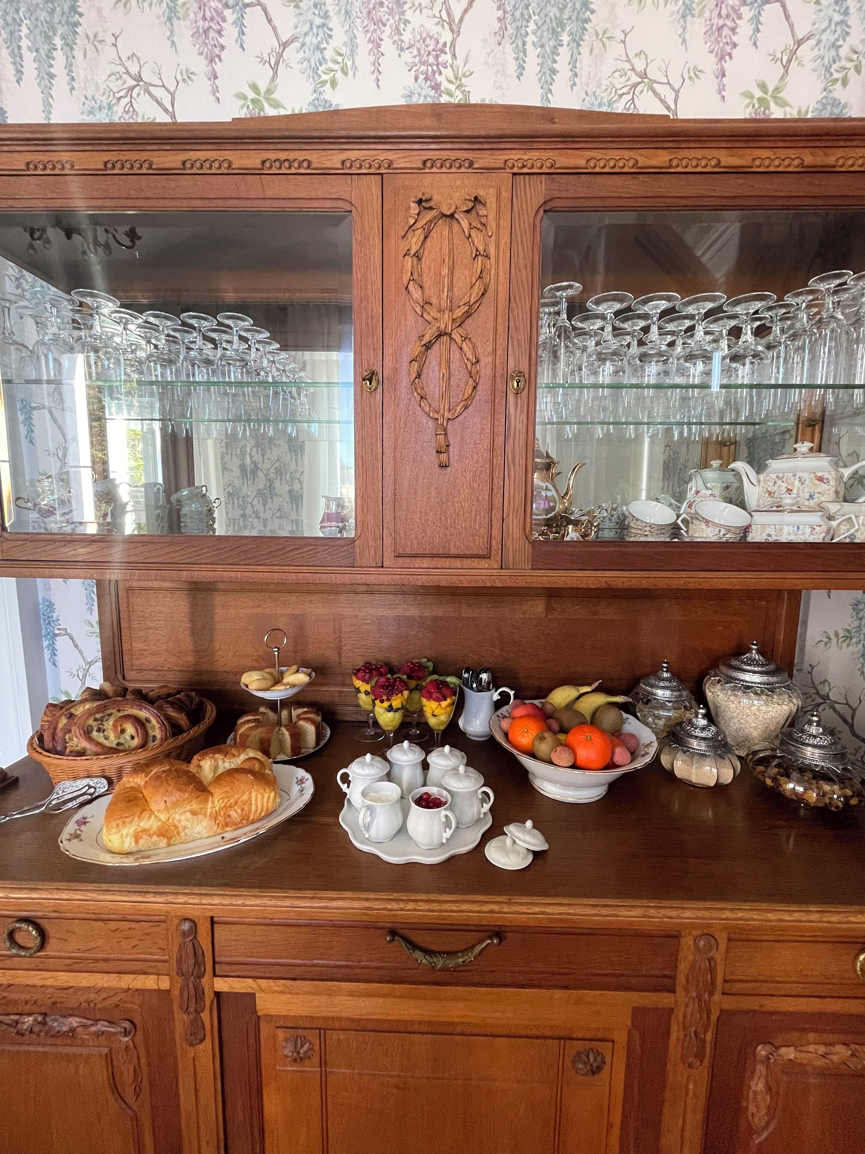 Een houten buffetkast met glazen deuren, gevuld met servies en glaswerk.