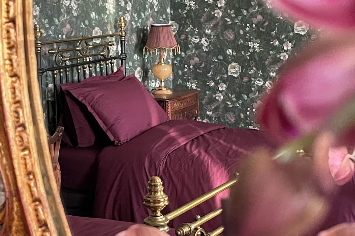 Un dormitorio con cama, mesita de noche, lámpara y papel tapiz floral.