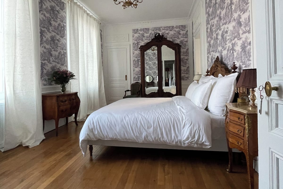 Un dormitorio con una cama grande, un aparador de madera, un espejo y una araña.