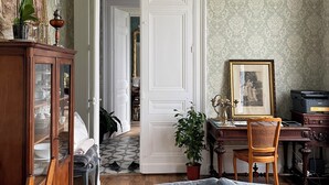 Una habitación con comedor, un sofá, un escritorio con silla y una puerta que da a otra habitación.
