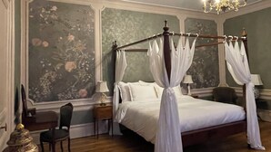 Un dormitorio con cama con dosel, candelabro y papel tapiz floral.