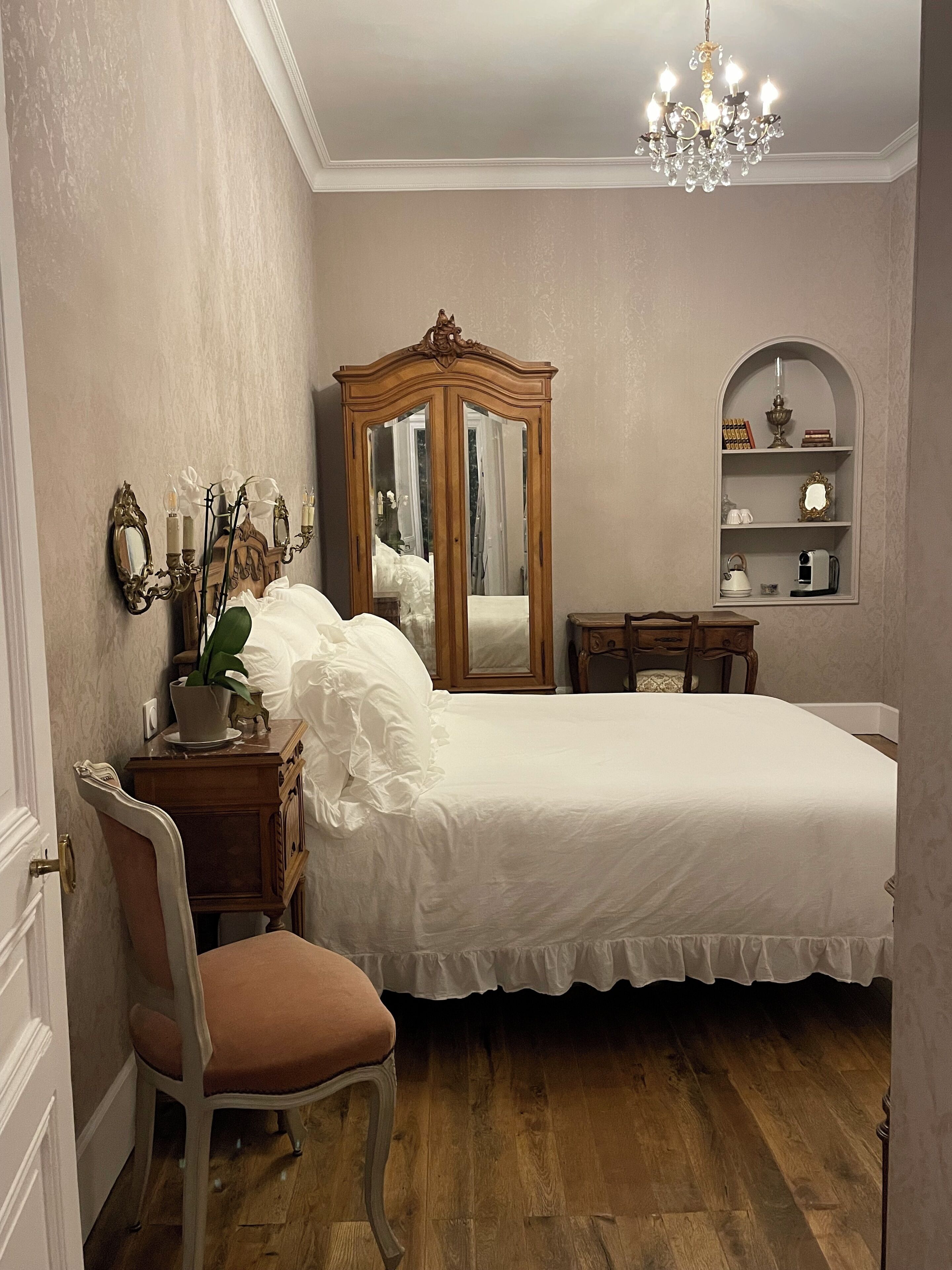 Quarto com cama, cadeira, cômoda, espelho e lustre.