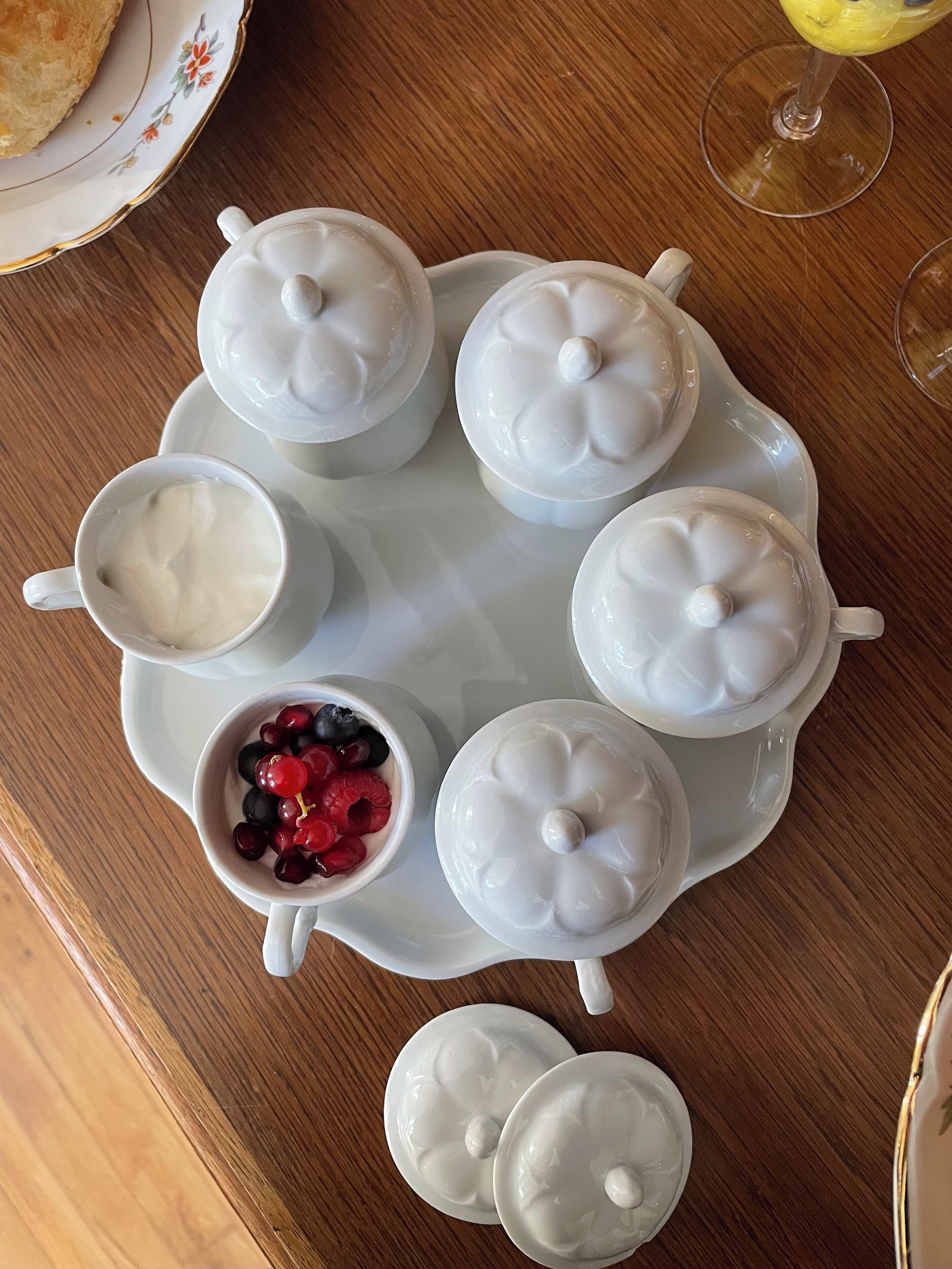 Une table sur laquelle sont disposés six récipients en céramique blanche, dont l’un contient une petite tasse et un bol rempli de fruits rouges variés.