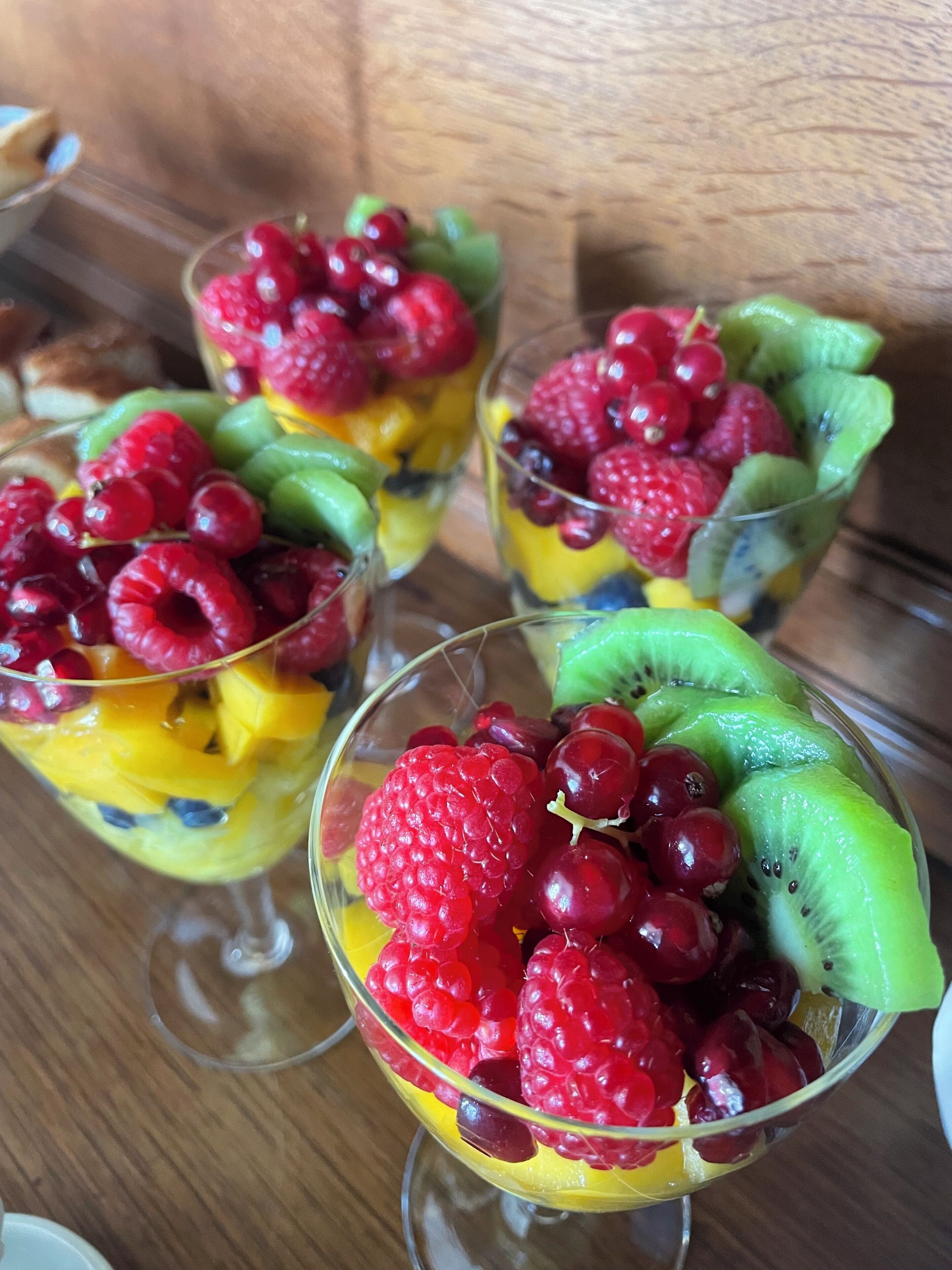 Tres vasos de ensalada de frutas con frambuesas, cerezas y rodajas de kiwi.