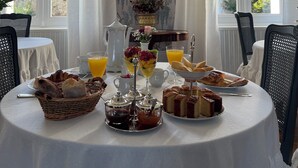 Una mesa de desayuno dispuesta con diversos alimentos y bebidas, un jarrón de flores y vistas al exterior a través de amplias ventanas.