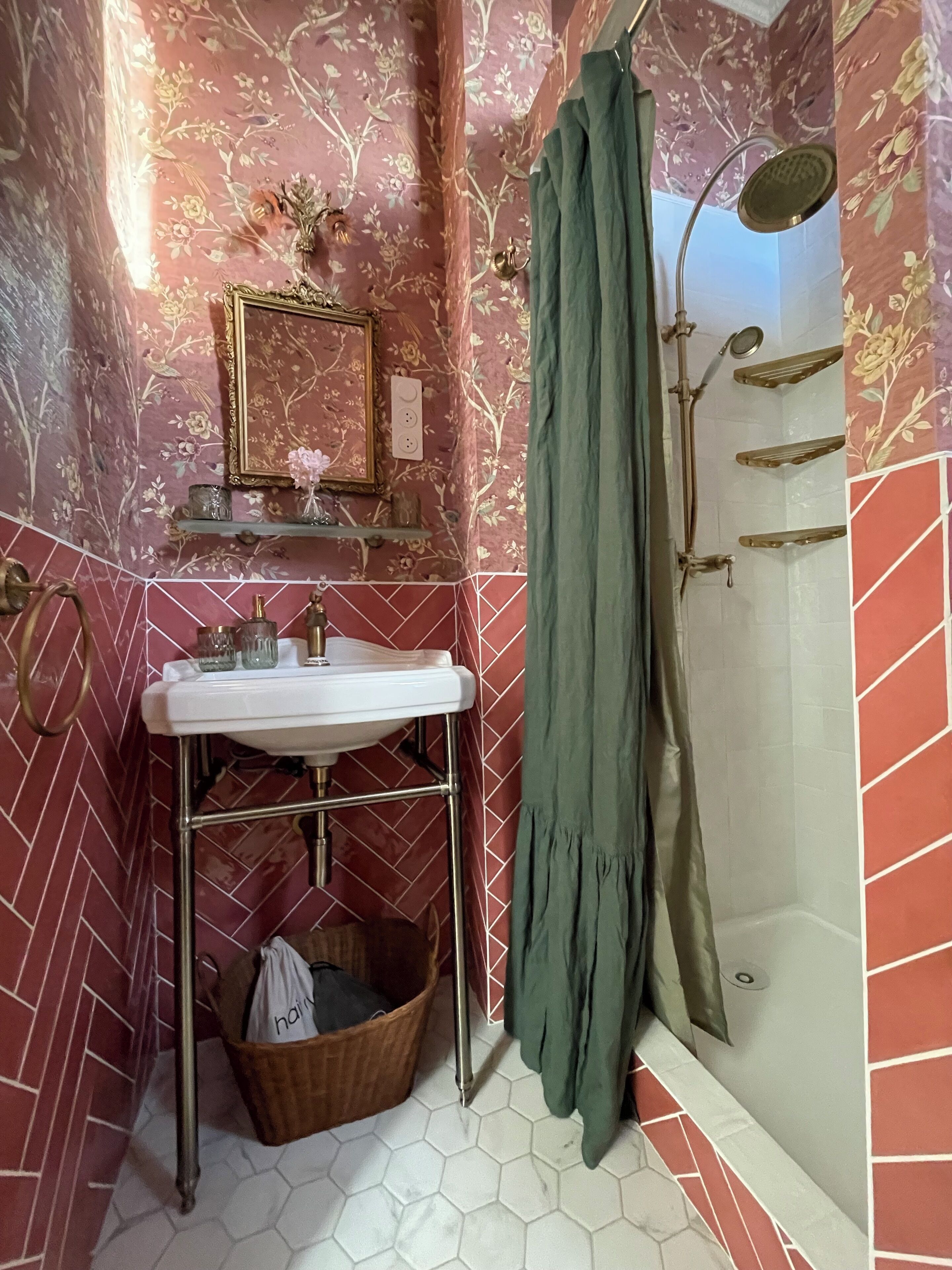 A bathroom with a sink, mirror, shower, and decorative floral wallpaper.