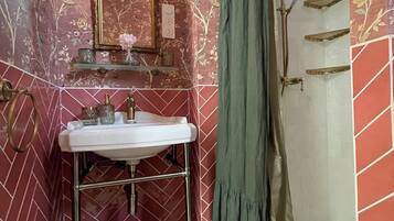 A bathroom with a sink, mirror, shower, and decorative floral wallpaper.