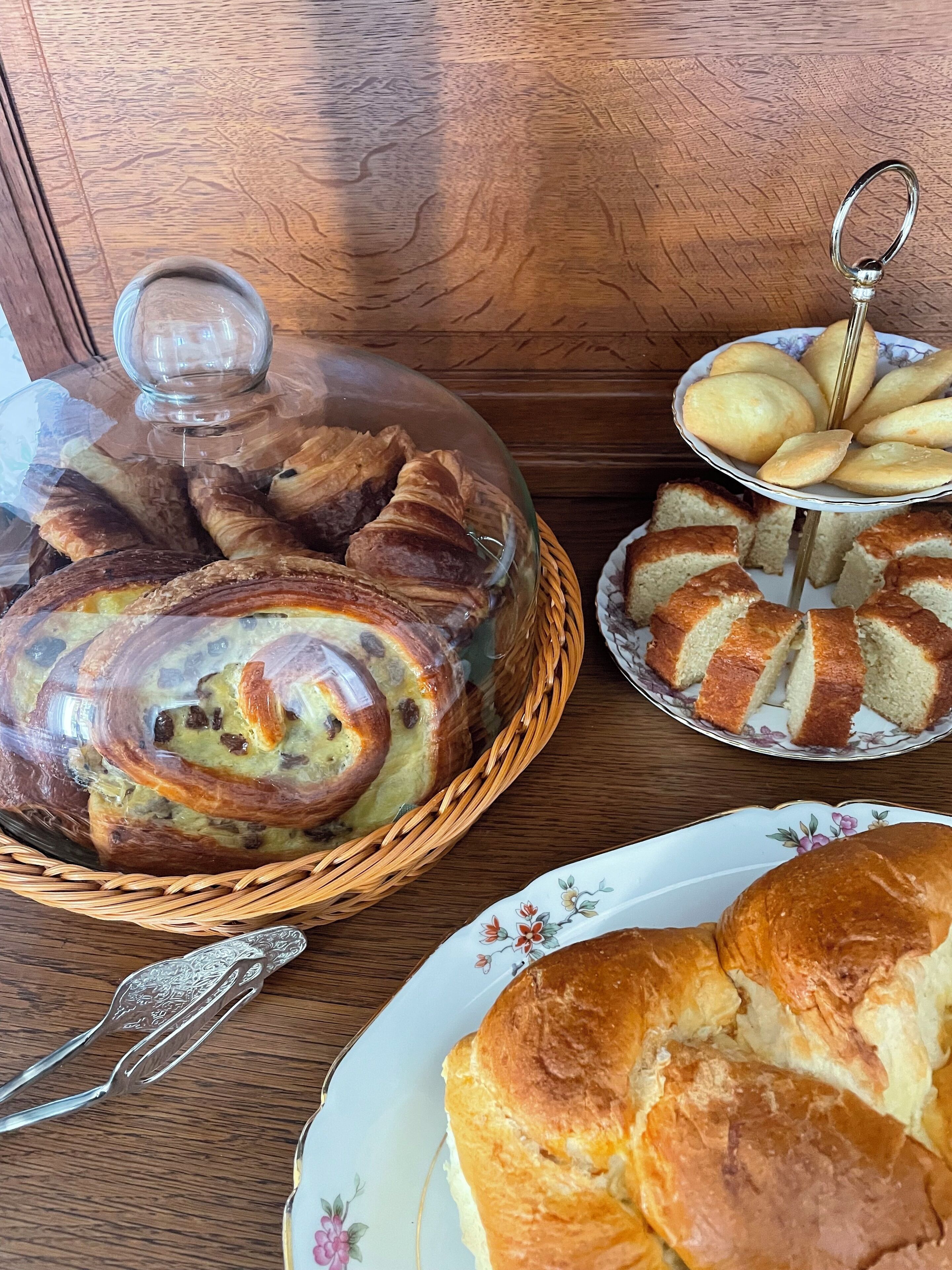 A wooden table with a variety of baked goods including bread, pastries, and a loaf of bread in a basket.