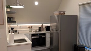 Een moderne keuken met een roestvrijstalen koelkast, een inbouwoven en een spoelbak. Op het aanrecht staat een kleine prullenbak en een potplant.