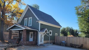 Een twee verdiepingen tellend huis met een stenen fundering, een overdekte veranda en een achtertuin met een barbecue.