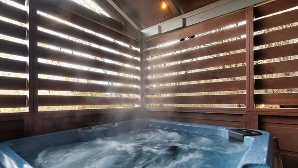 Un bain à remous où s'échappe de la vapeur, entouré de lattes de bois et éclairé par un luminaire au plafond.