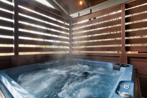 Un jacuzzi con vapor que se eleva, rodeado de listones de madera y una luz en el techo.