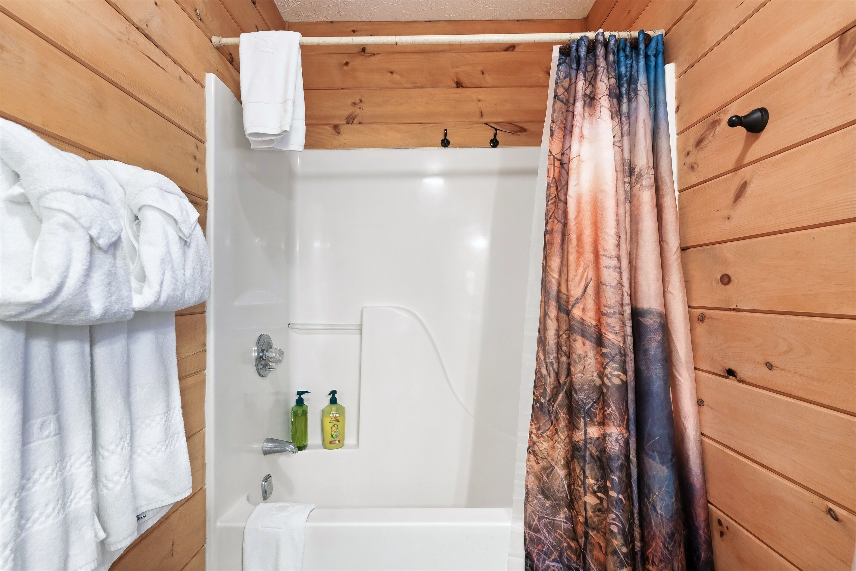 Een badkamer met houten lambrisering, een badkuip, douchegordijn en twee shampoo flessen.