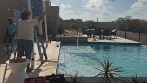 Une piscine avec un espace patio, un parasol blanc et quelques personnes assises autour.
