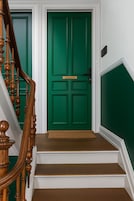 Una escalera con barandillas de madera que conduce a una puerta verde con picaporte y una placa.