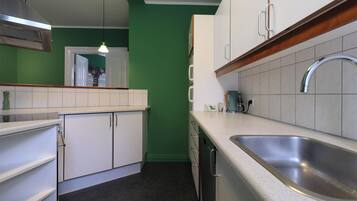 Una cocina con armarios blancos, un lavamanos de acero inoxidable y una pared verde.