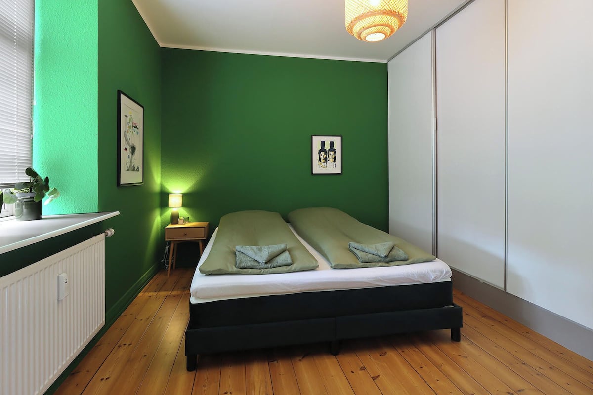 A room with a bed, a nightstand, a lamp, and a framed picture on the wall.