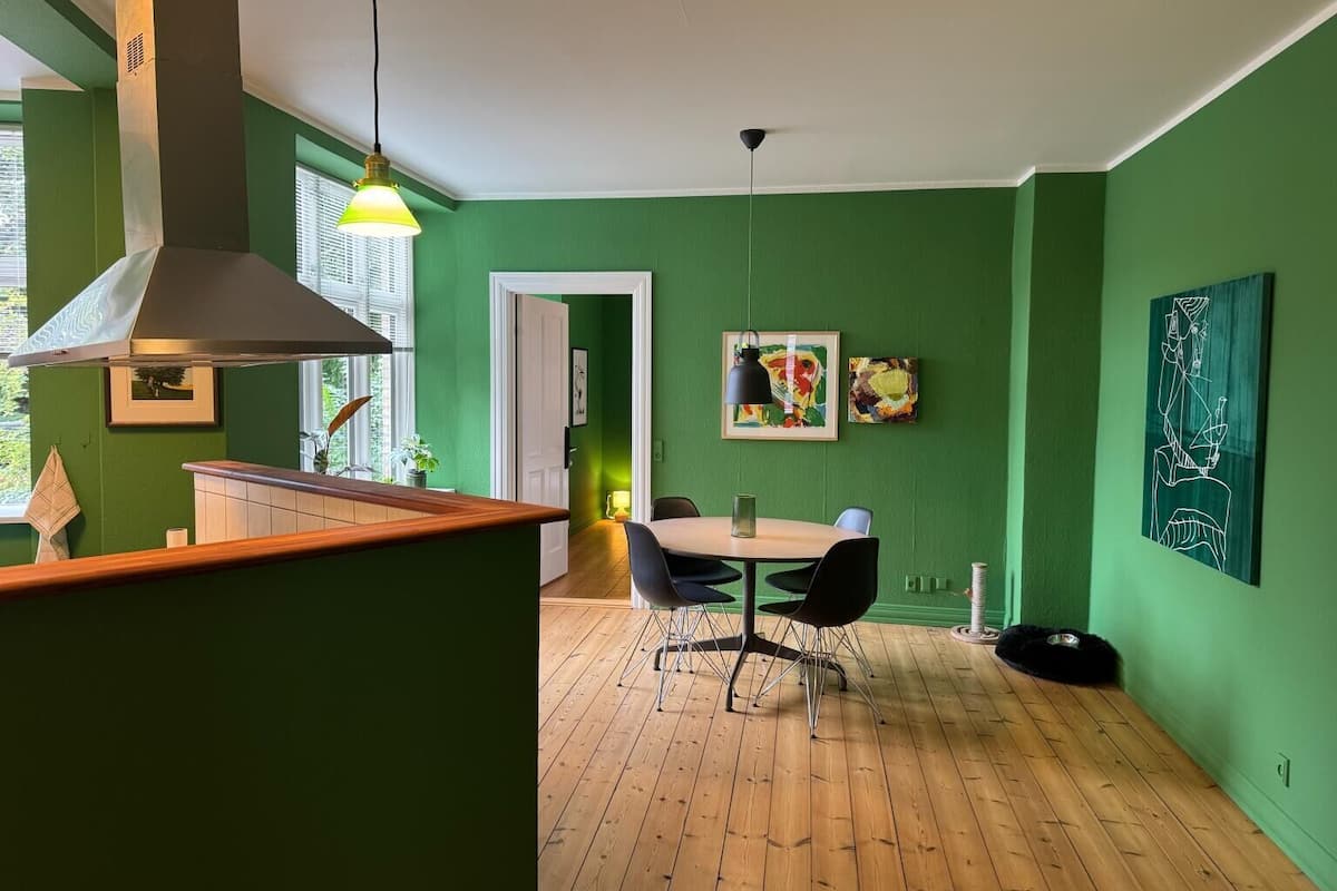 Una cocina moderna con pared verde, suelo de madera y un comedor con mesa y sillas.